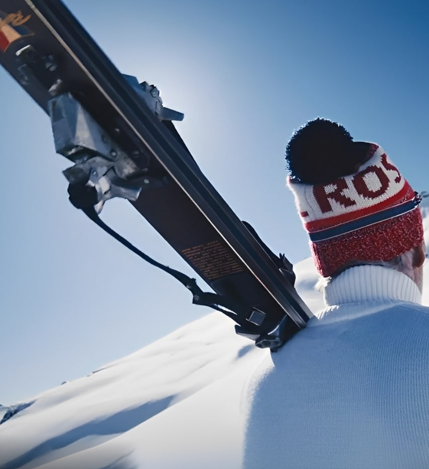 Un homme de dos portant des skis Rossignol